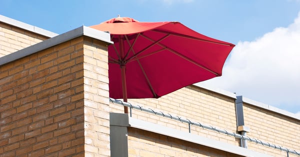 På bilden syns en husfasad med ett rött parasoll på en balkong. Fasaden är i gult tegel.