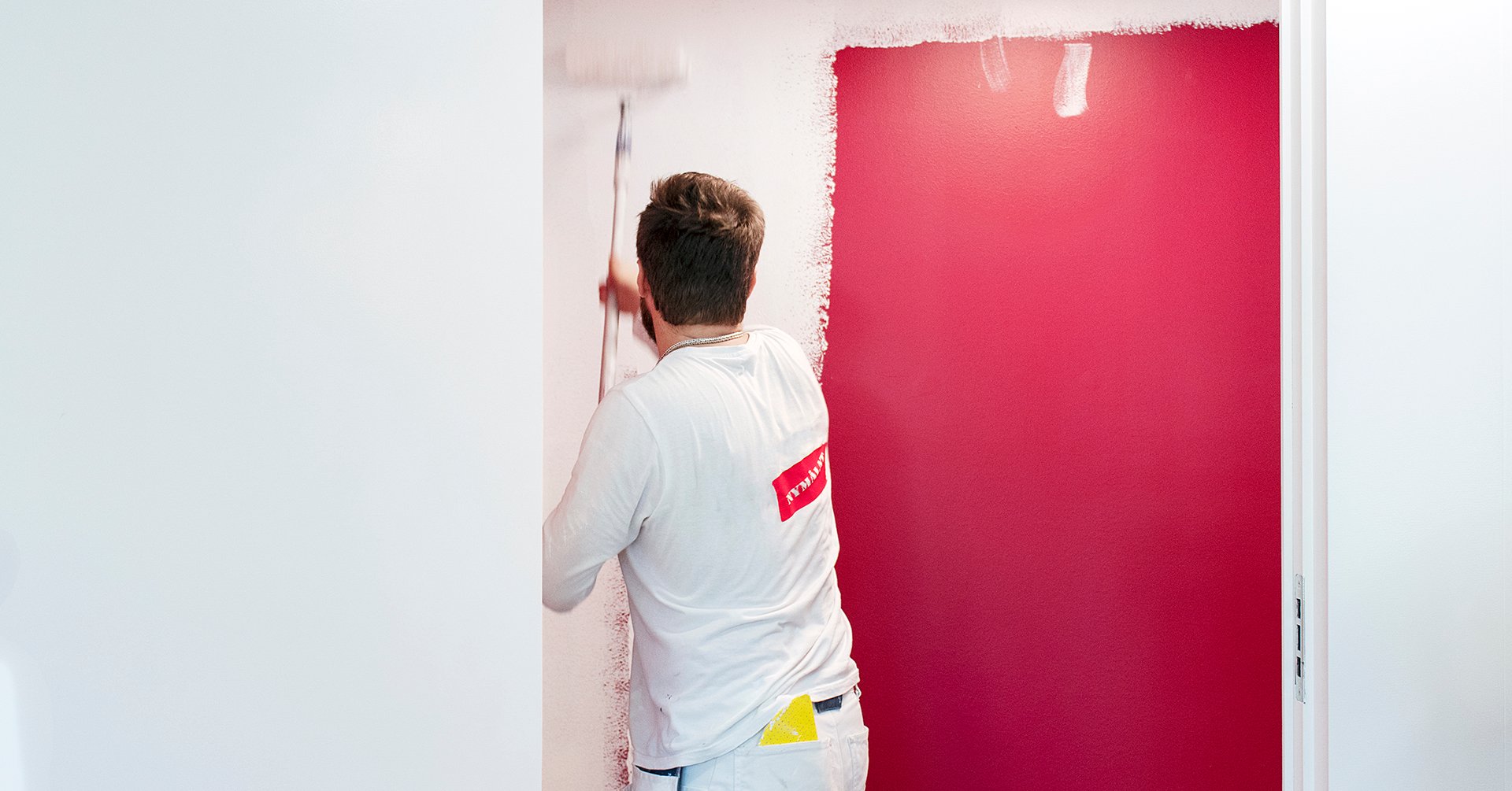 På bilden sysn en målare i vitt som målar en vitvägg röd.