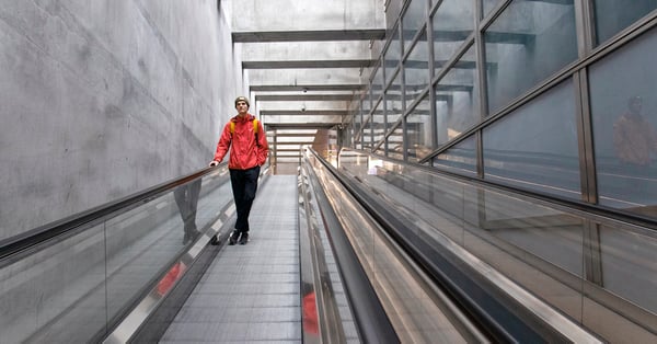 På bilden syns en man i röd jacka som åker i en rulltrappa.