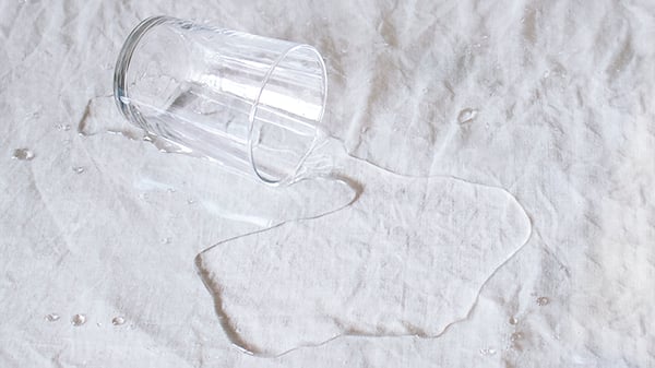 På bilden syns ett glassvatten som läckt ut över en vit duk.