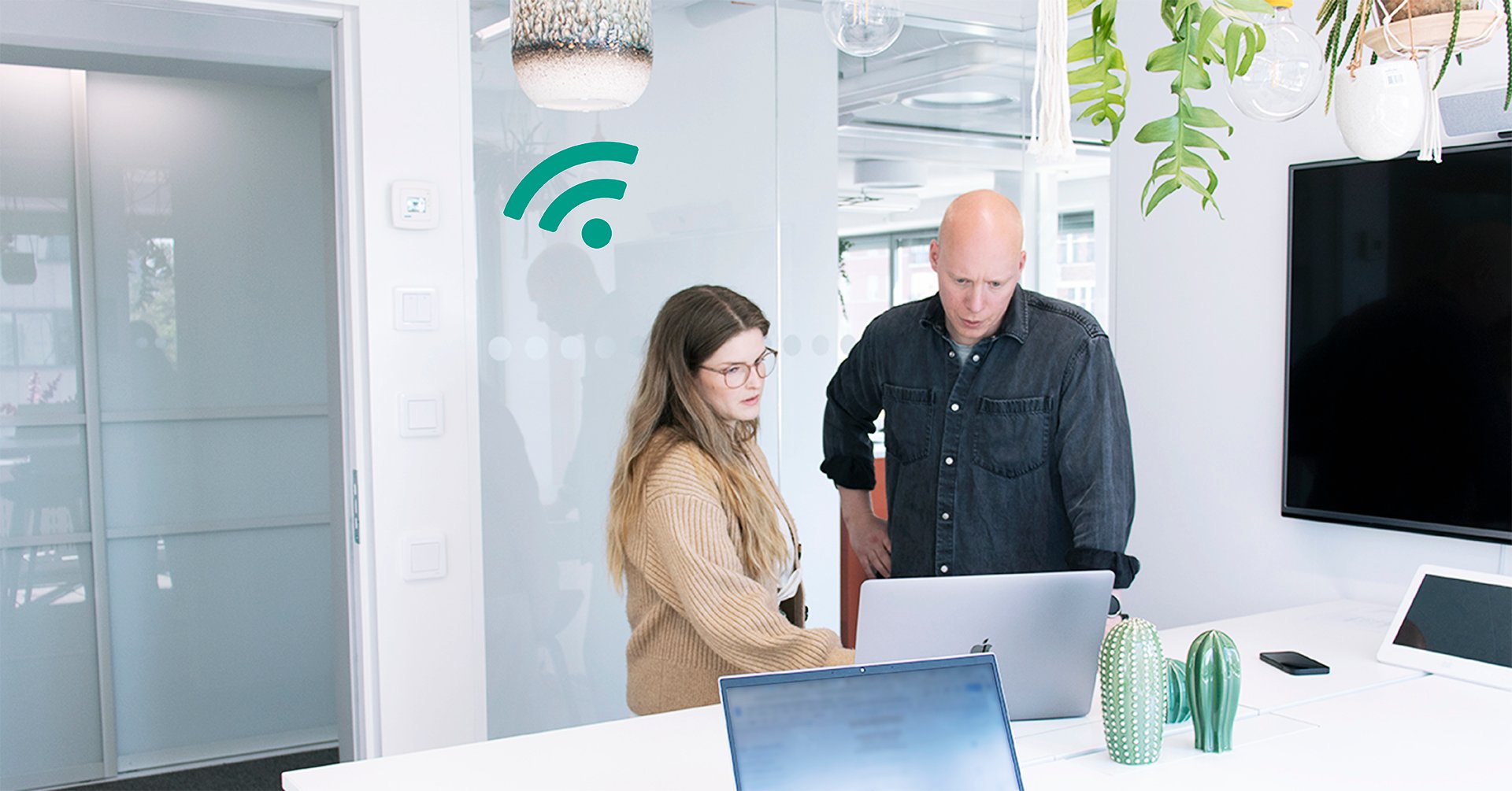 På bilden syns ett kontorsrum med en kvinna i brun tröja och en man i svart skjorta. De står lutade över en laptop och ser bekymrade ut.