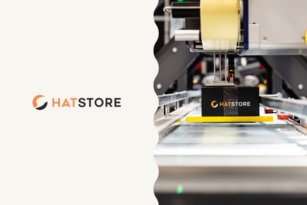 Bild på Hatstore:s logotyp samt foto från deras lager på en kartong på ett produktionsband