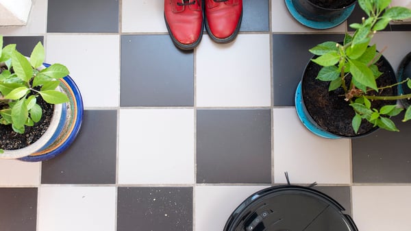På bilden syns ett shackrutigt golv med röda skor och en robotdammsugare.