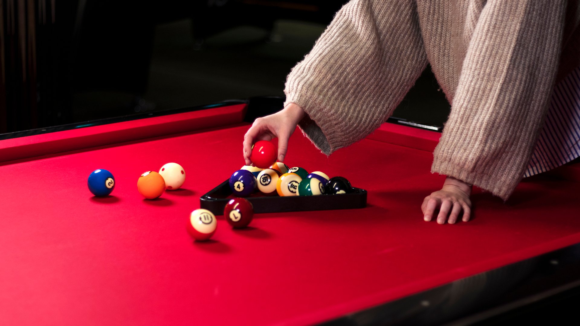 På bilden syns ett biljardbord med röd matta och två armar som ställer bollarna i ordning.