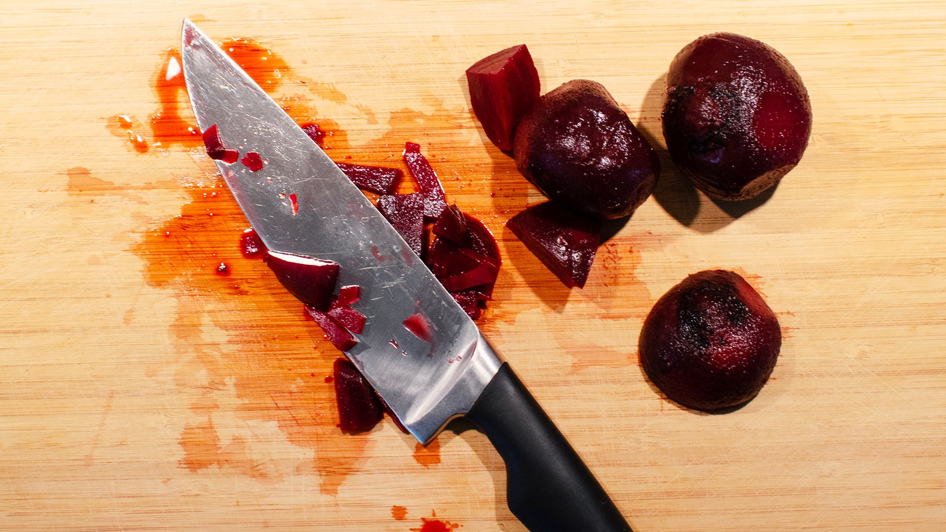 På bilden syns en kökskniv liggandes på en skärbräda med hackade rödbetor runt omkring.