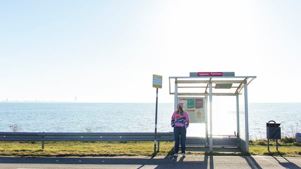 På bilden syns en unga kvinna vid en busshållplats med namnet Upptech framtiden.