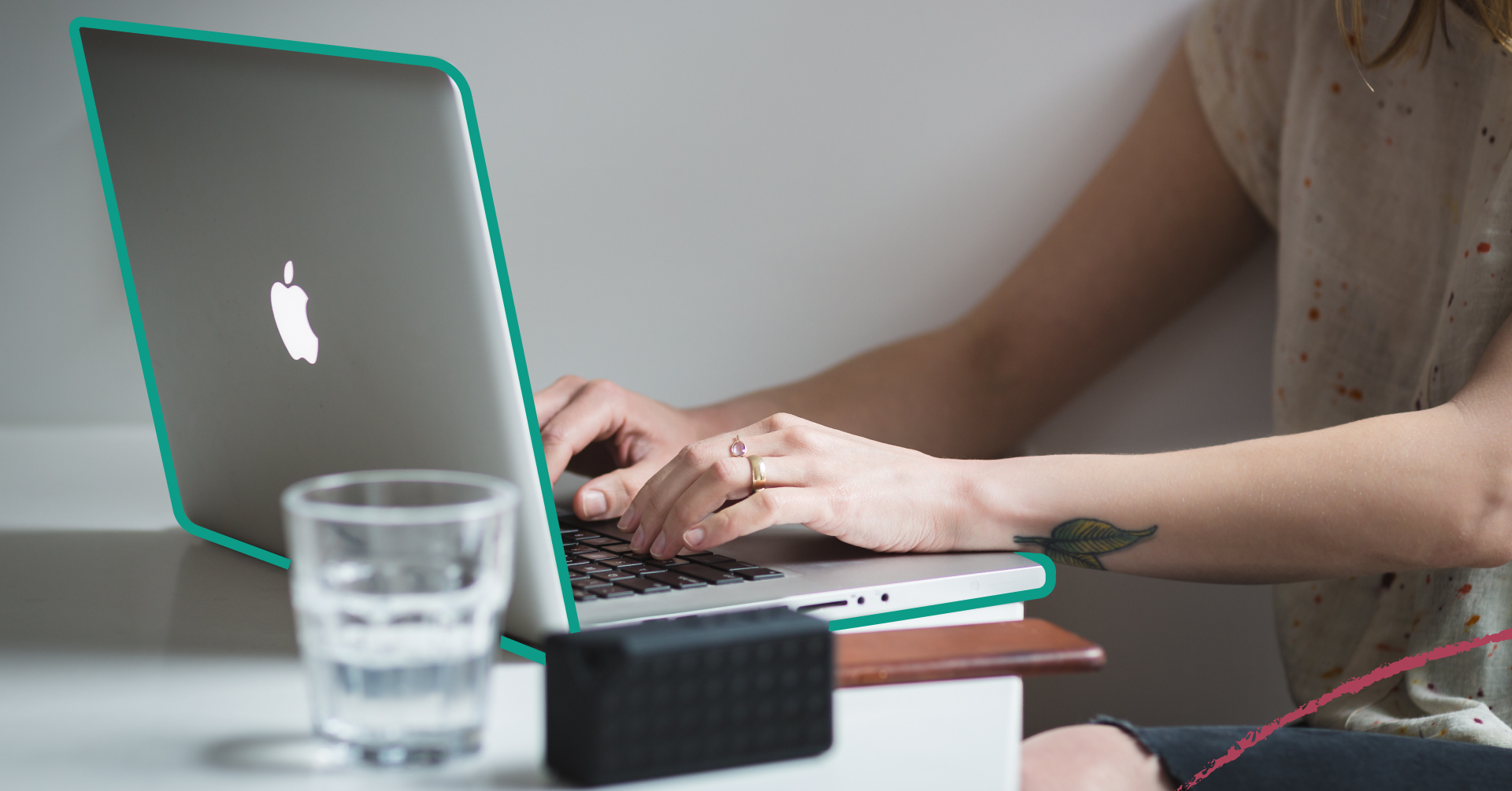 Fotografi på en persons händer som skriver på en laptop. På bordet står det ett glas vatten och en laptop.